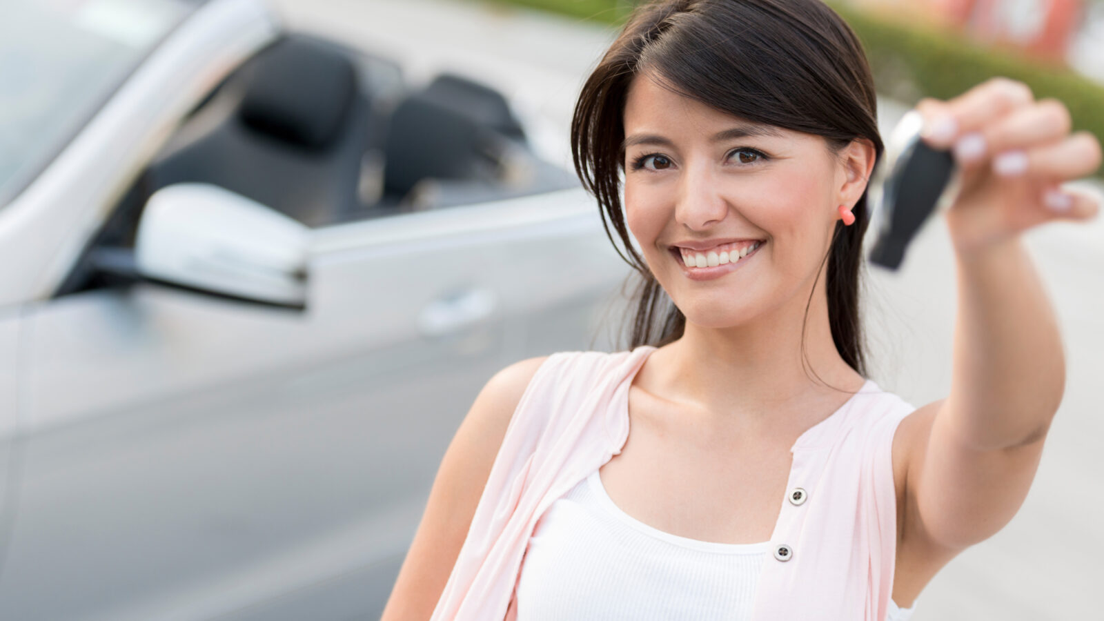 Young woman smiling while holding car keys in front of a white sedan