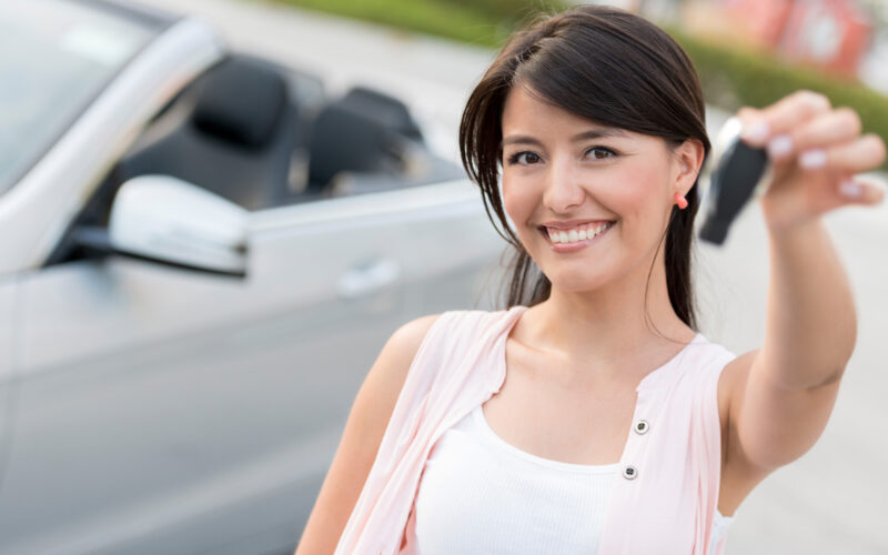 Young woman smiling while holding car keys in front of a white sedan